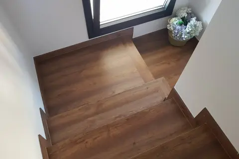Escaleras con suelo laminado de madera, con un cesto de flores junto a una ventana.
