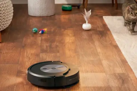 Un Roomba con error 17 se detiene en un suelo de madera. Un gato observa desde una alfombra.