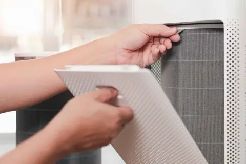 Persona saca un filtro HEPA de un purificador de aire para limpiarlo.