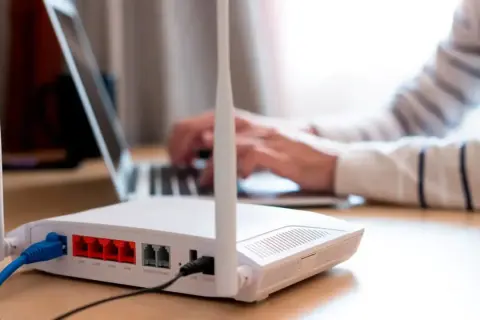 Persona frustrada intenta conectar un portátil a un router que no se enciende. Cables azules y negros conectados.