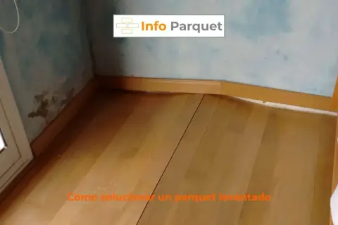 Parquet bufado en una esquina, con marcas de humedad en la pared. Se muestra cómo solucionar un parquet levantado.