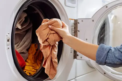 Mano saca ropa de lavadora. Un truco para limpiar lavadora con vinagre es añadirlo al ciclo de lavado.