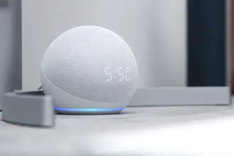 Altavoz inteligente Echo Dot con pantalla mostrando la hora. La luz azul indica que está listo para recibir ayuda de la app Alexa.