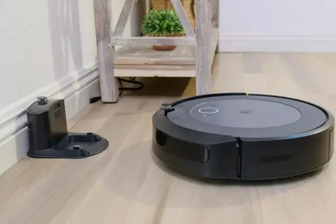 Aspiradora robot negra junto a su base de carga, lista para un mapeo rápido del hogar.
