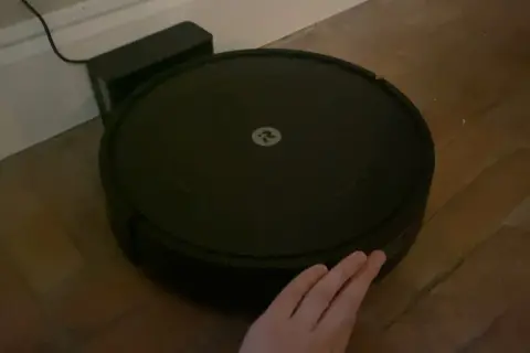 Robot aspirador Roomba con logo, conectado a su base. Una mano intenta interactuar, pero parece que hay un error 47.