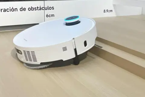 Robot aspirador blanco sobre suelo laminado, superando un pequeño desnivel.