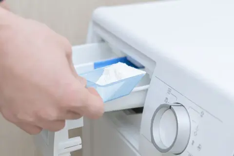 Mano agrega detergente en polvo a la lavadora.