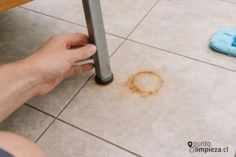 Mano levantando pata de mueble para mostrar cómo quitar manchas de óxido en el suelo de baldosas.