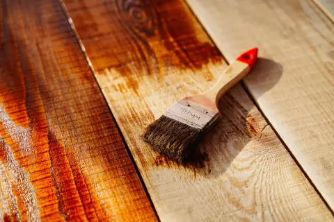 Brocha aplicando barniz a tablones de madera, resaltando el brillo y la veta.