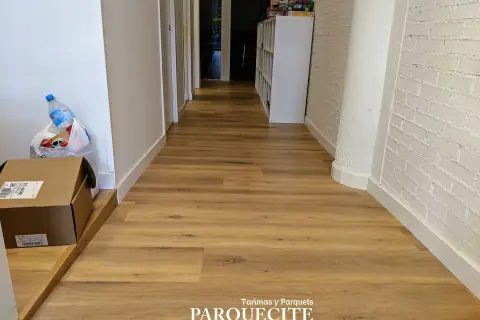 Pasillo con tarima de madera, ideal para saber como colocar tarima en pasillos. Se ven cajas y una botella de agua.