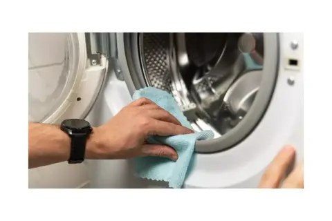 Mano limpiando la goma de la lavadora para eliminar el mal olor.