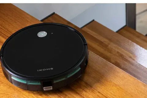 El robot aspirador Netbot S15, negro y redondo, se desliza por escalones de madera pulida, listo para limpiar.