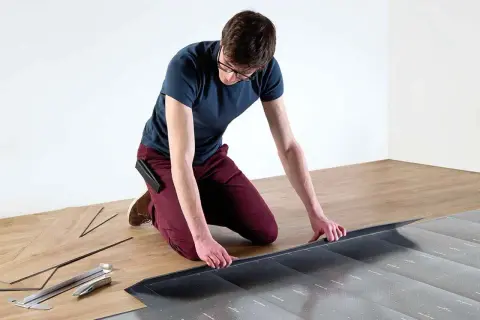 Hombre con gafas instalando suelo laminado sin experiencia. Herramientas y lamas de madera a su lado.