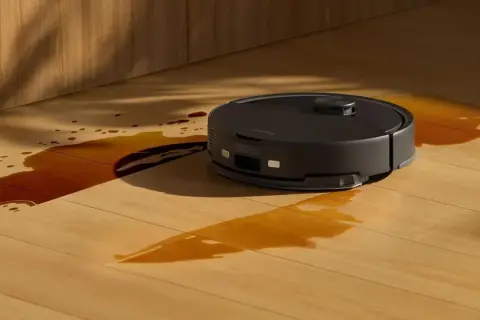 Robot aspirador negro limpiando un derrame de líquido marrón en un suelo de madera. ¿Cuánto dura un robot aspirador?