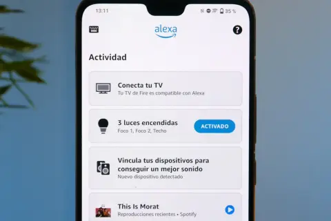 Pantalla de móvil con la app Alexa. Muestra "Actividad", "Conecta tu TV", "3 luces encendidas" (activado) y "This Is Morat". Parece que Alexa no funciona bien.