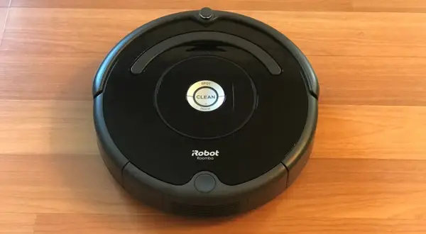 Un robot aspirador Roomba, uno de los modelos antiguos, descansa sobre un suelo de madera.