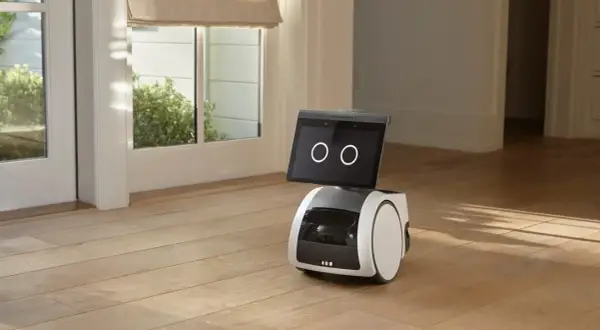El robot Alexa Astro, con pantalla y ruedas, se encuentra en un suelo de madera, cerca de una puerta acristalada.