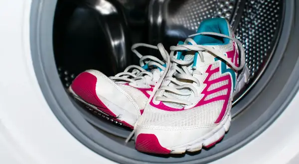 Un par de deportivas blancas con detalles fucsia y turquesa listas para lavar en lavadora.