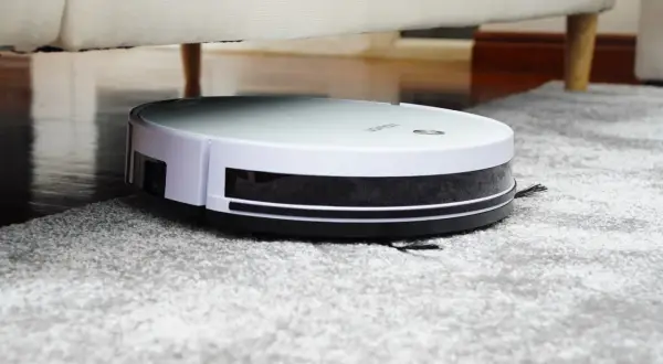 Robot aspirador Rowenta en alfombra gris, bajo un sofá. Las opiniones sobre este robot son muy positivas.