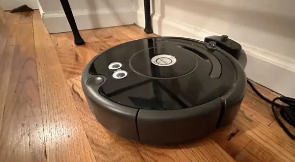 Robot aspirador negro sobre suelo de madera, parece que el roomba no detecta la base de carga.