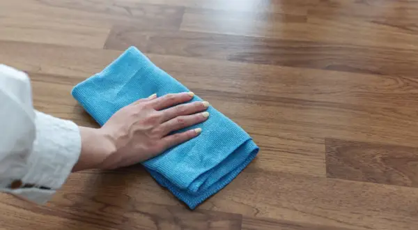 Mano con paño azul limpiando suelo laminado, ideal para saber como limpiar suelo laminado después de obra y dejarlo impecable.