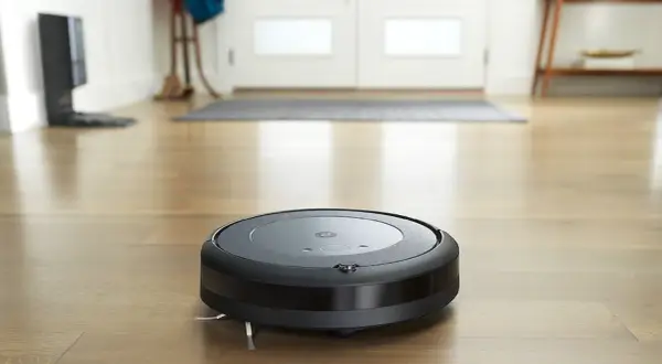 Un Roomba i3 negro aspira el suelo de madera.