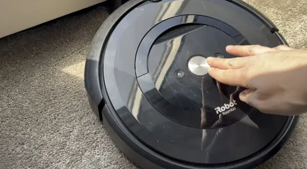 Mano presionando el botón "CLEAN" en un Roomba e5, quizás por **roomba e5 problemas**.