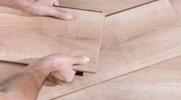 Manos desmontando una tabla de suelo laminado.