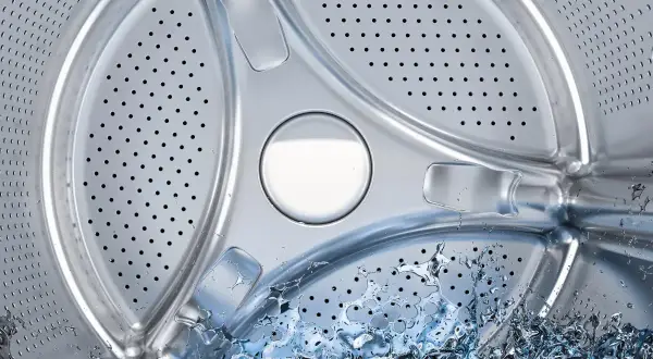 Interior de lavadora con agua salpicando. Averigua cuántos litros gasta una lavadora para optimizar tu consumo.