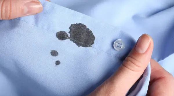 Manos sostienen una camisa azul con manchas de tinta. Aprende como quitar las manchas de tinta de la ropa.