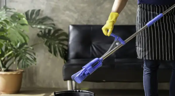 Persona con guantes amarillos y delantal a rayas friega el suelo con una mopa azul.