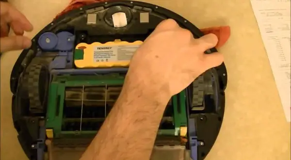 Mano arreglando un Roomba con **error 15**. Se ve la batería amarilla y las escobillas.