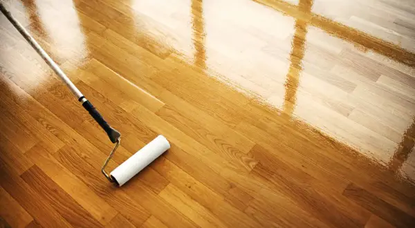 Rodillo aplicando barniz a un suelo de madera. El mantenimiento del parquet es esencial para su brillo y durabilidad.