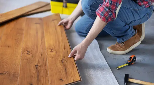 Persona instala parquet flotante de madera, colocando una tabla sobre otra.
