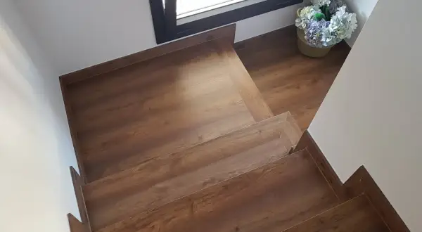 Escaleras con suelo laminado de madera, con un cesto de flores junto a una ventana.