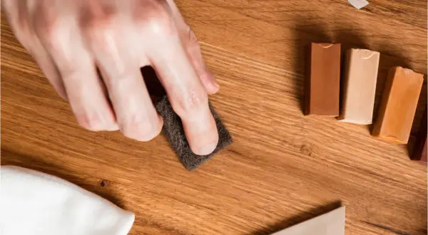 Mano lijando para reparar suelo laminado. Cera de colores y espátula listas para el retoque.