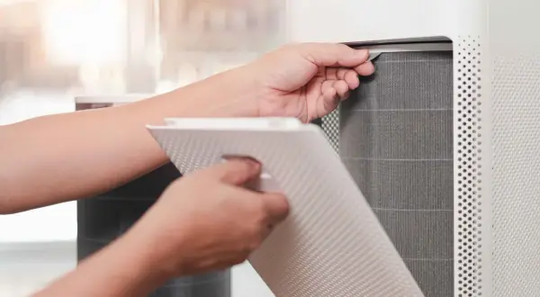 Persona saca un filtro HEPA de un purificador de aire para limpiarlo.