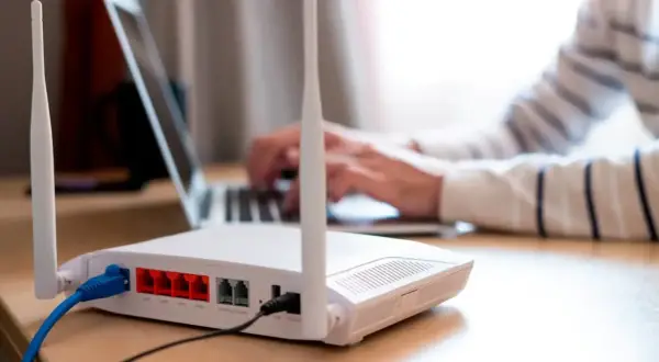 Persona frustrada intenta conectar un portátil a un router que no se enciende. Cables azules y negros conectados.