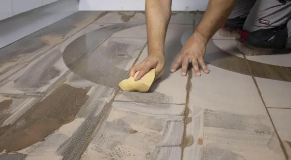 Man limpiando un suelo de baldosas con una esponja amarilla. Se ve el proceso de con que se friega el suelo.