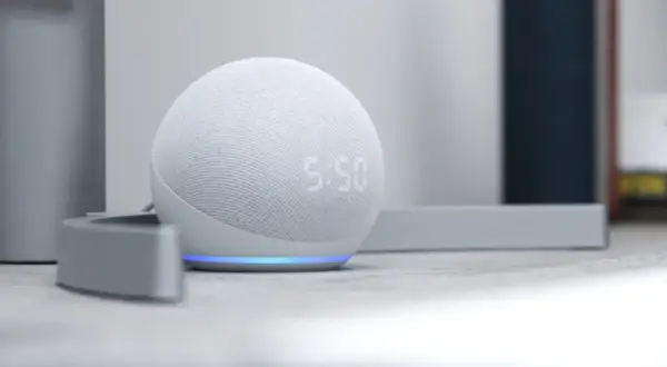 Altavoz inteligente Echo Dot con pantalla mostrando la hora. La luz azul indica que está listo para recibir ayuda de la app Alexa.