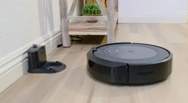 Aspiradora robot negra junto a su base de carga, lista para un mapeo rápido del hogar.