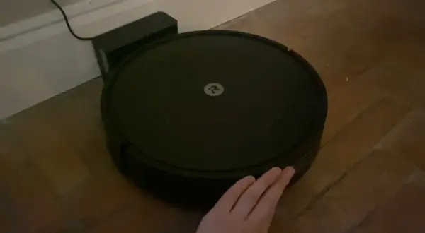 Robot aspirador Roomba con logo, conectado a su base. Una mano intenta interactuar, pero parece que hay un error 47.