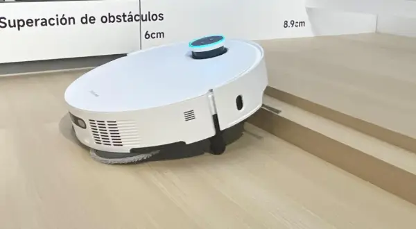 Robot aspirador blanco sobre suelo laminado, superando un pequeño desnivel.