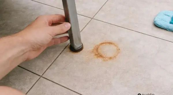 Mano levantando pata de mueble para mostrar cómo quitar manchas de óxido en el suelo de baldosas.