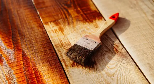 Brocha aplicando barniz a tablones de madera, resaltando el brillo y la veta.