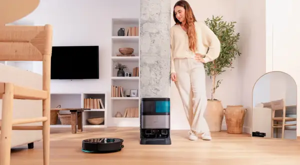 Una mujer sonríe junto a su nueva conga, un robot aspirador que limpia el suelo mientras ella descansa.