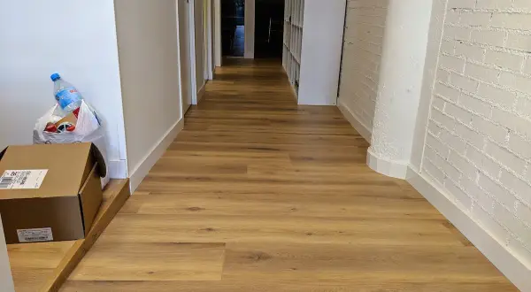 Pasillo con tarima de madera, ideal para saber como colocar tarima en pasillos. Se ven cajas y una botella de agua.