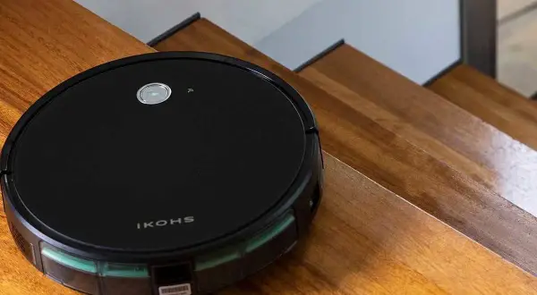 El robot aspirador Netbot S15, negro y redondo, se desliza por escalones de madera pulida, listo para limpiar.