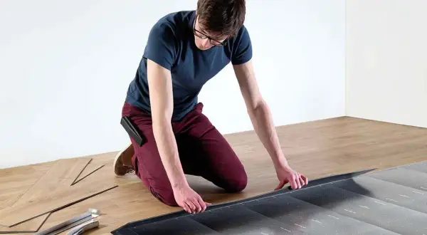Hombre con gafas instalando suelo laminado sin experiencia. Herramientas y lamas de madera a su lado.