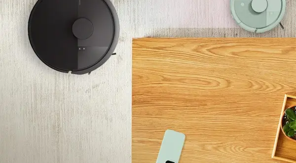 Dos robots aspiradores, uno negro y otro verde, limpian la alfombra. El negro parece tener una irobot bolsa, listo para recoger el polvo.